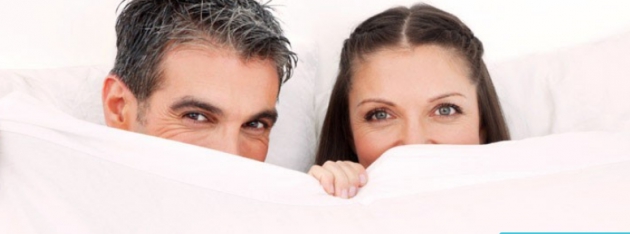 Mann und Frau hinter einer weißen Bettdecke von BettenTrend
