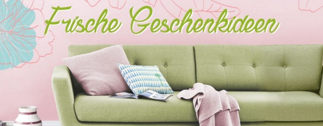 Frische Geschenkideen - Grünes Sofa mit Kissen vor roséfarbenem Hintergrund